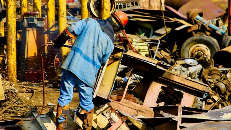 Ouvrier découpant du métal dans une casse automobile pour recyclage.